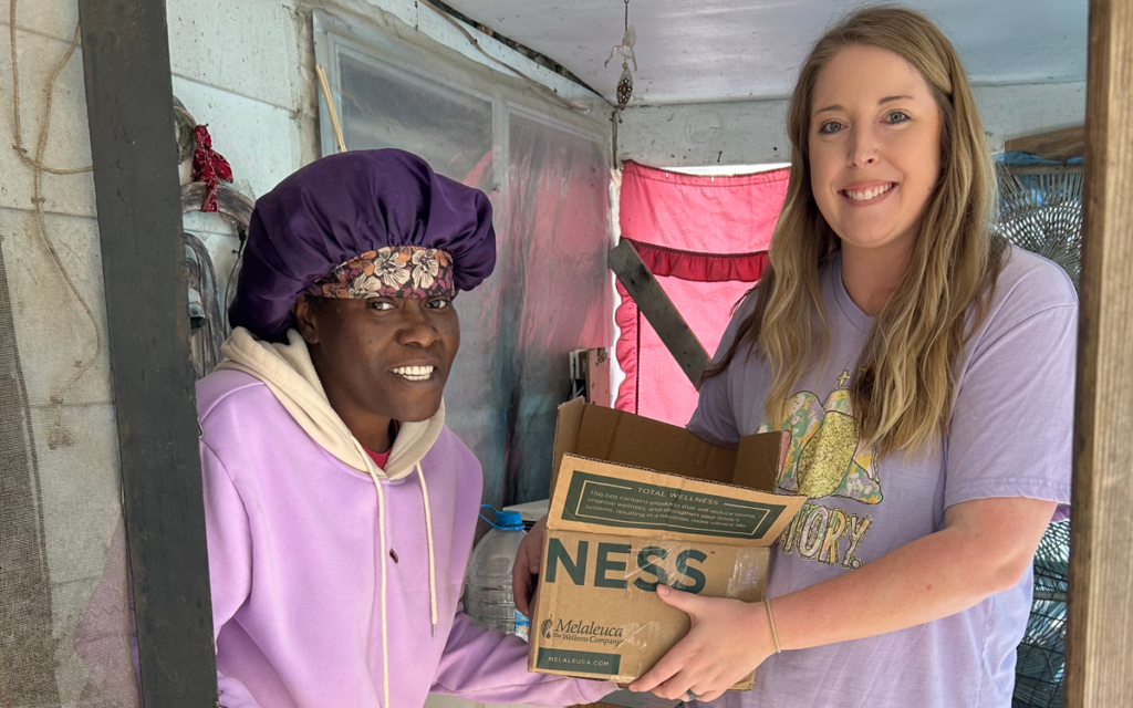 Representative holding a box of Melaleuca products while standing next to a storm victim in Missouri.